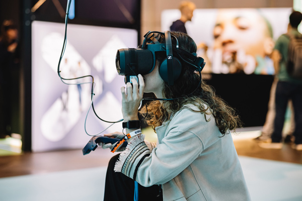 A person wearing a VR headset crouches down. In their right hand, they hold a VR controller. Their left hand is lifted towards their face, as if about to adjust the headset. They're viewed in profile.