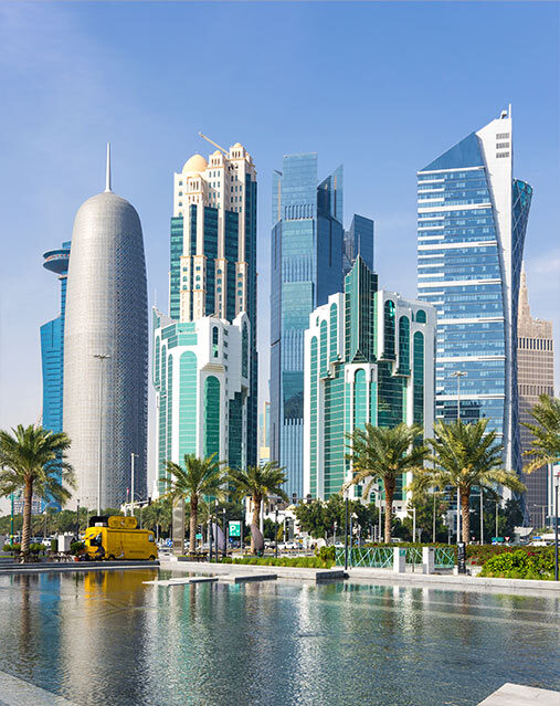 A cluster of modern glass skyscrapers. At the base of the skyscrapers, palm trees line a pool of water.