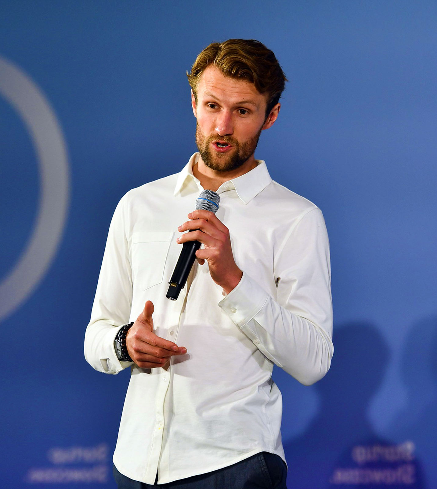 A photograph of a startup pitch on Startup Showcase stage. The person is holding a microphone and appears to be speaking. They are standing up.