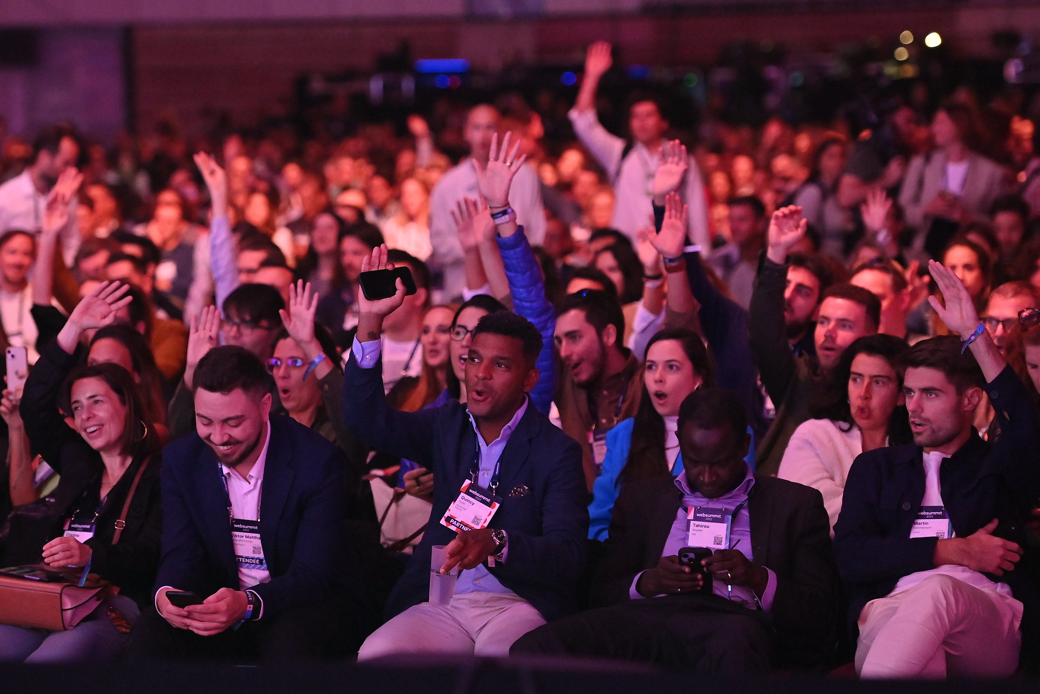 A crowd of dozens of attendees raise their hands as they face the Centre Stage at Web Summit 2022 at the Altice Arena in Lisbon