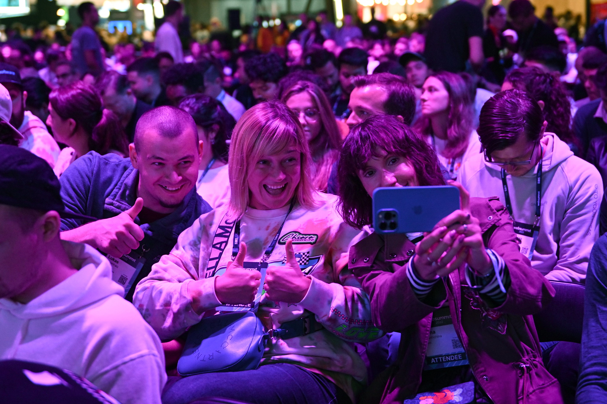 Three smiling people pose for a selfie. They are sitting in a crowded audience.