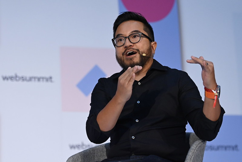 A person (Initialized Capital founder Garry Tan) sits in an armchair. Garry, who appears to be speaking, is wearing a headset mic and gesturing with both hands, as if to indicate how high something is. On the wall behind Garry, the Web Summit logo is visible in several places.