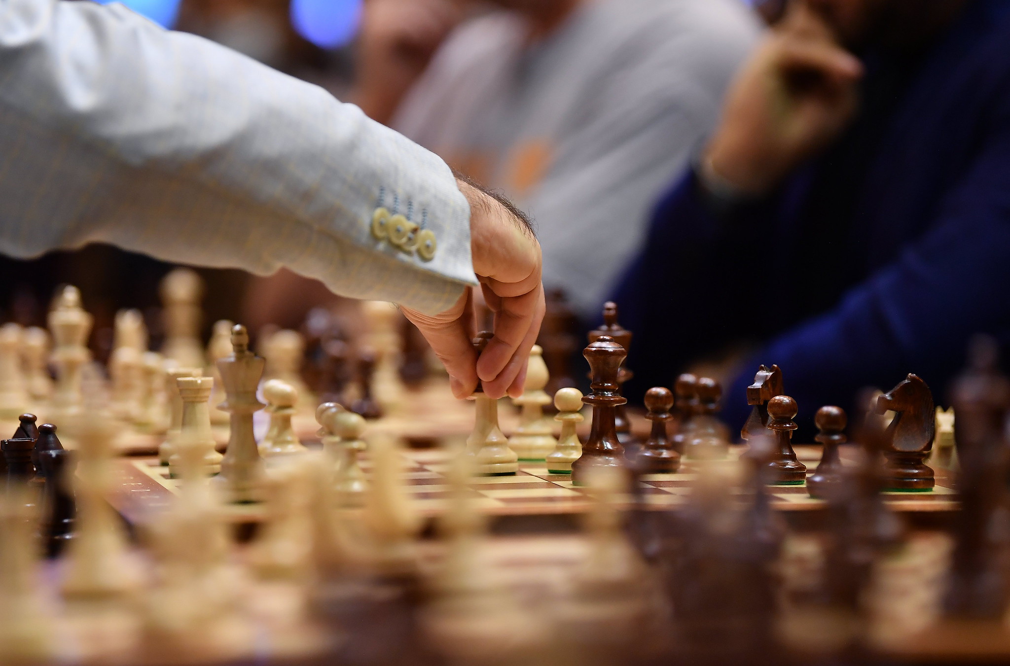Close up of a game of chess with the focus on a hand holding the white queen in the centre of the board