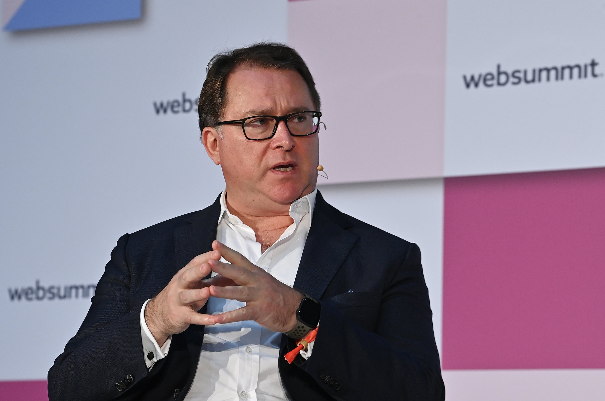 A person (DN Capital founder and managing partner Nenad Marovac) pictured from the waist up. The person is holding their fingertips together in a tented style. They are wearing a headset mic and appear to be speaking. The Web Summit logo is visible in several places on the wall behind them.