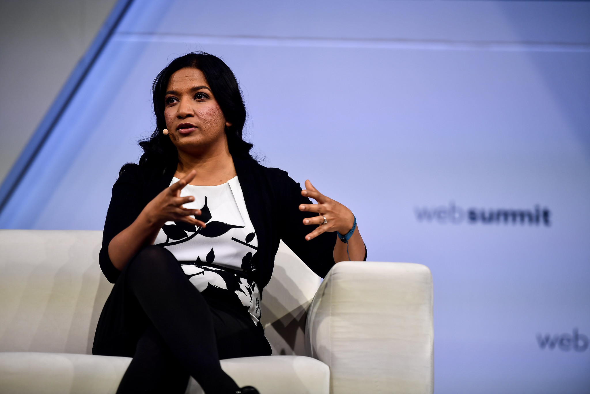 Rashmi Gopinath is pictured sitting on a couch giving a talk on FullSTK stage at Collision 2019. Rashmi appears to be wearing a microphone and is motioning with their hands. The Web Summit logo appears on the wall in the background.
