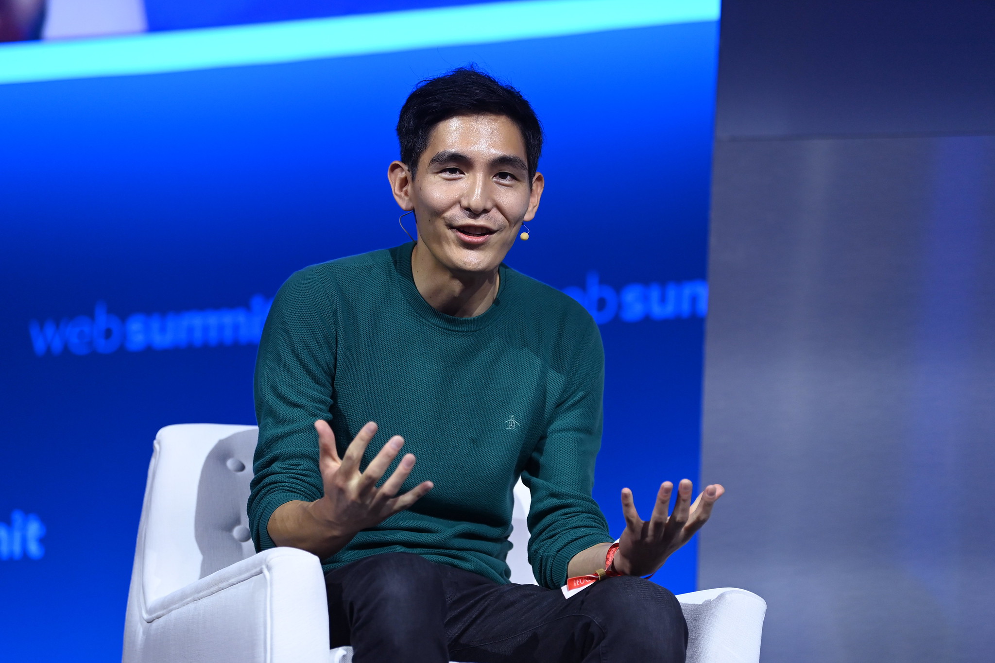 Photograph of a person (Yuhki Yamashita, chief product officer of Figma) speaking on stage at Web Summit. They are sitting on a chair and gesturing with their hands. They are wearing an on-ear microphone.