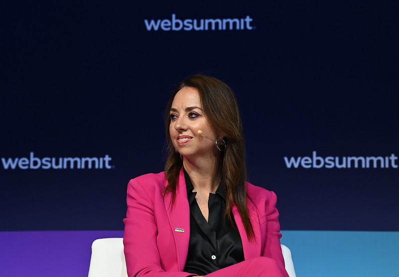 Photograph of a person (Jamie Domenici, former CMO of GoTo) sitting on a chair on stage at Web Summit. They are wearing an on-ear microphone. The Web Summit logo is visible in the background.