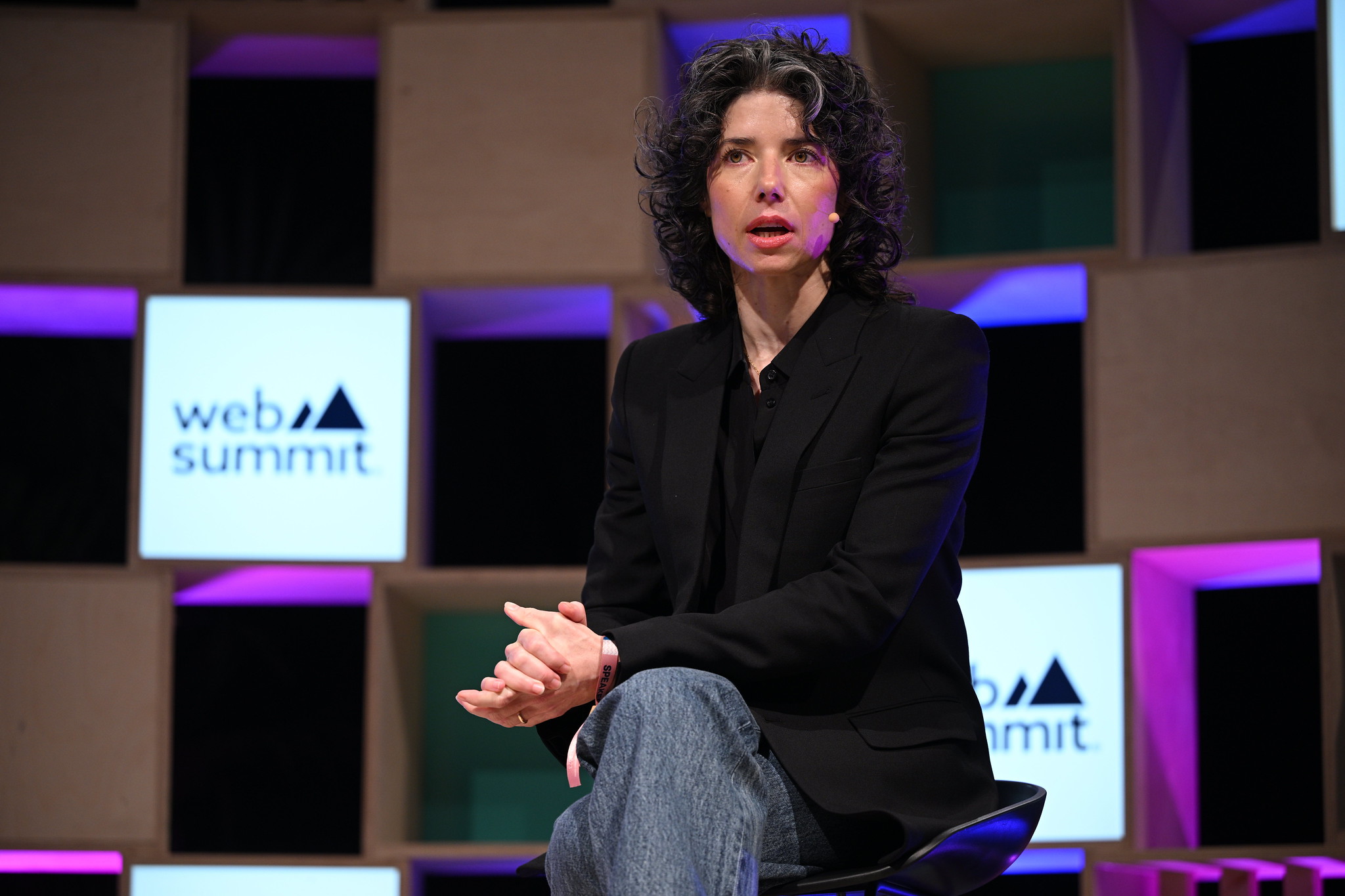 Photograph of a person (Meredith Whittaker, president of Signal) speaking on stage at Web Summit. The person is sitting on a chair. They are wearing a headset and appear to be speaking.