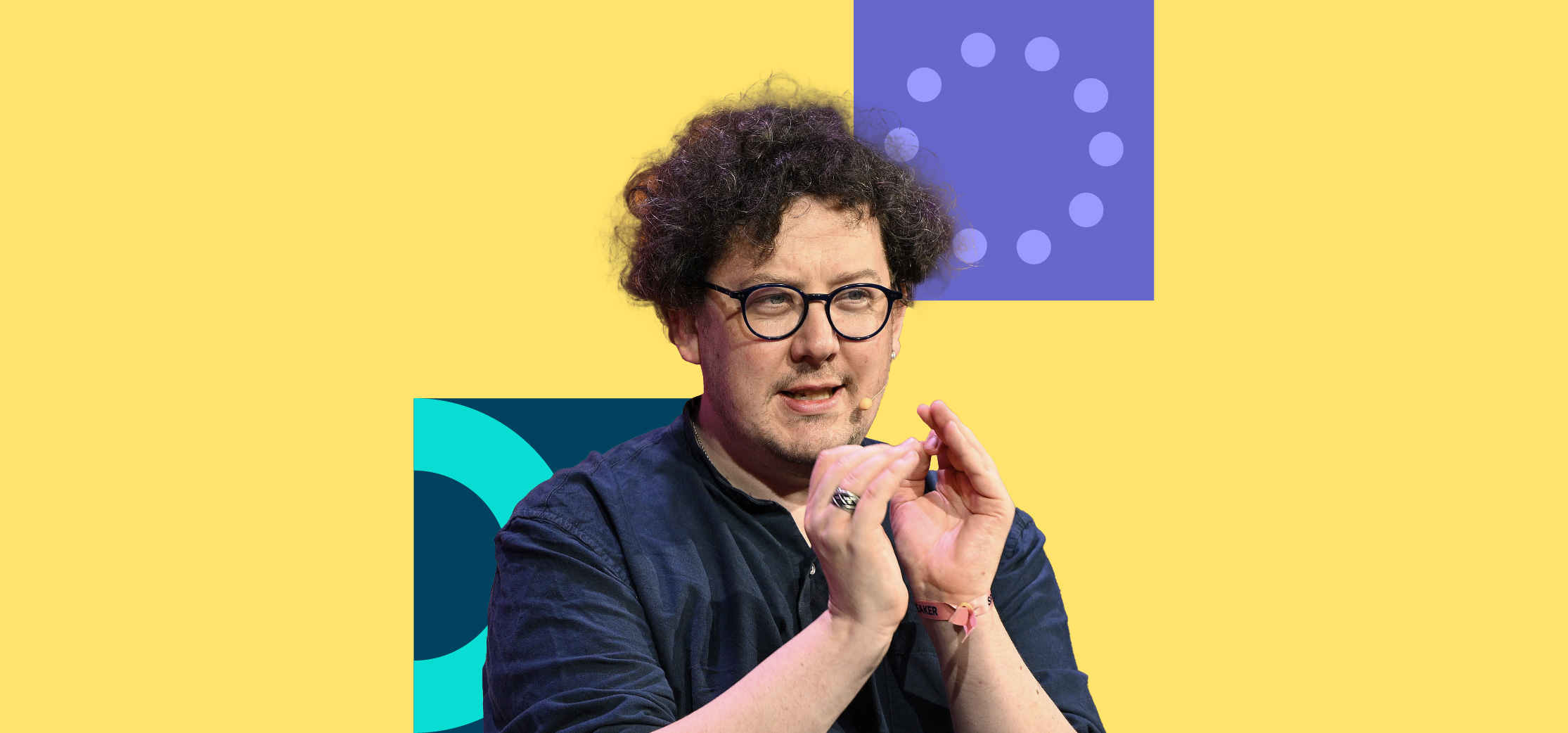 A photograph of a person (James Ball, journalist) speaking on stage at Web Summit 2023. They are gesturing with their hands. The photograph is on top of a solid background with two small square blocks, one with a ring of solid circles and the other with a block ring.