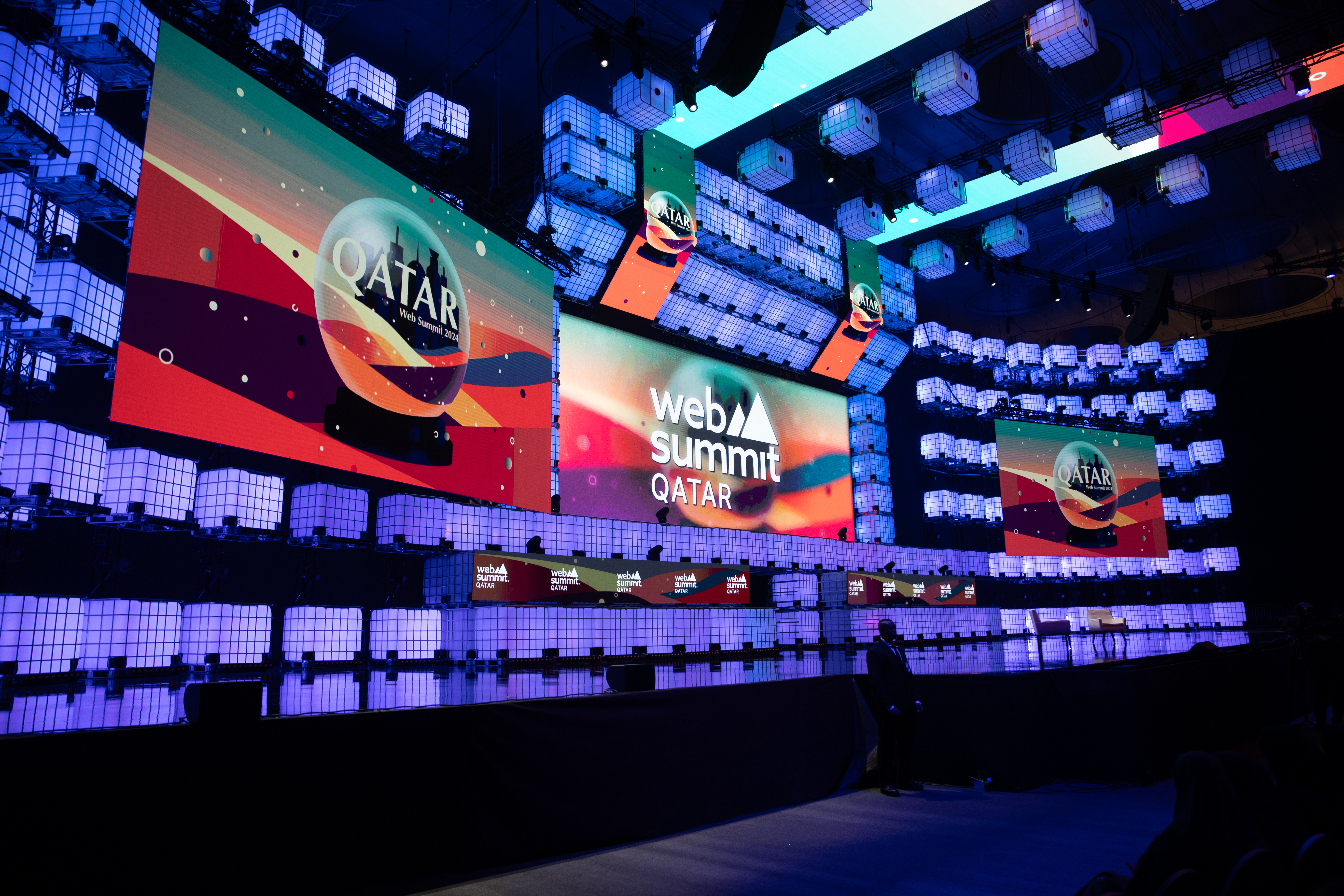 A photo of Centre Stage at Web Summit Qatar. There are three screens on the stage with the Web Summit Qatar logo visible.