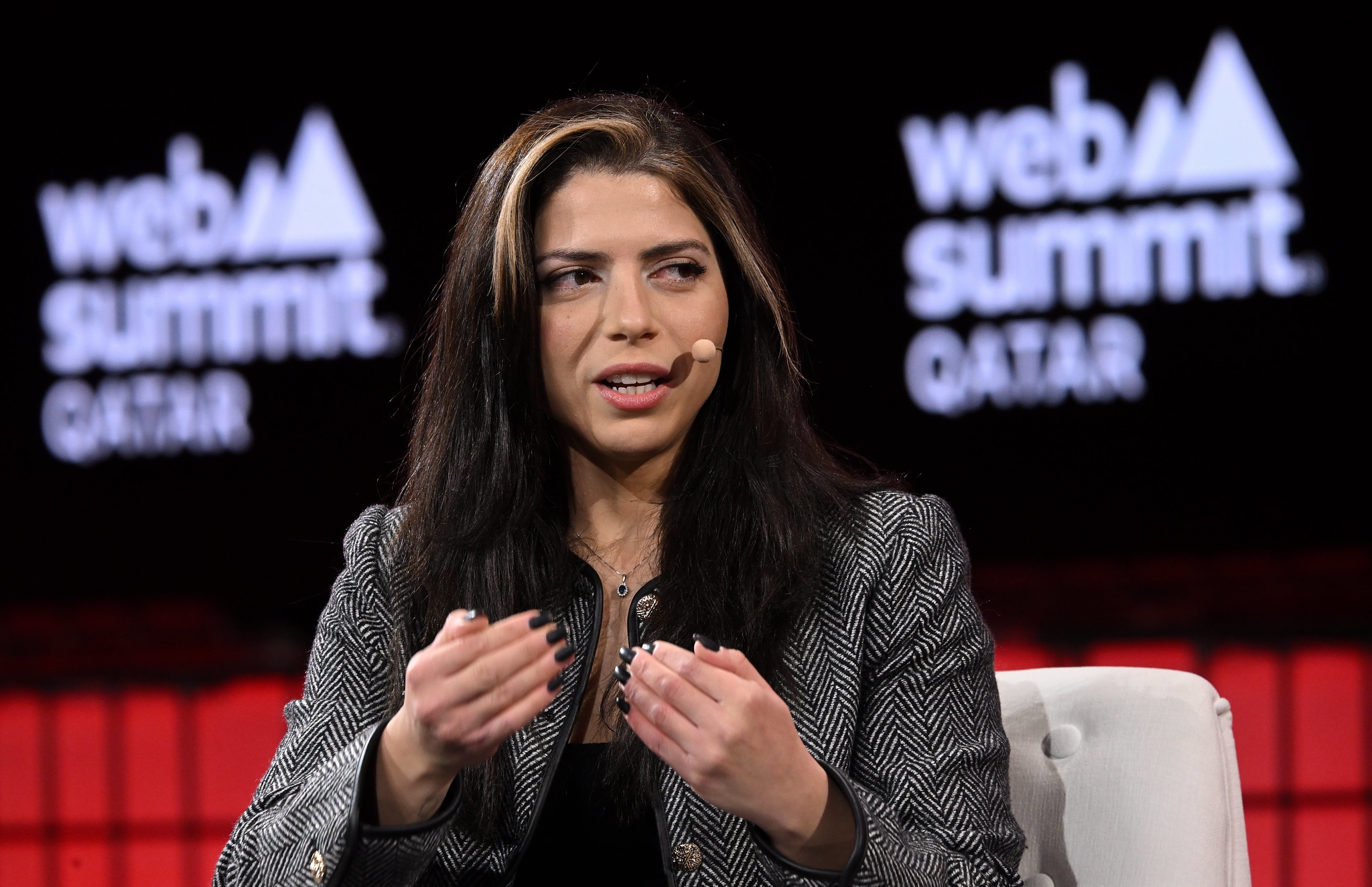A photograph of Sara Sabry, founder, CEO and astronaut at Deep Space Initiative, on stage at Web Summit Qatar 2024. She is gesturing with her hands and wearing a headset microphone.