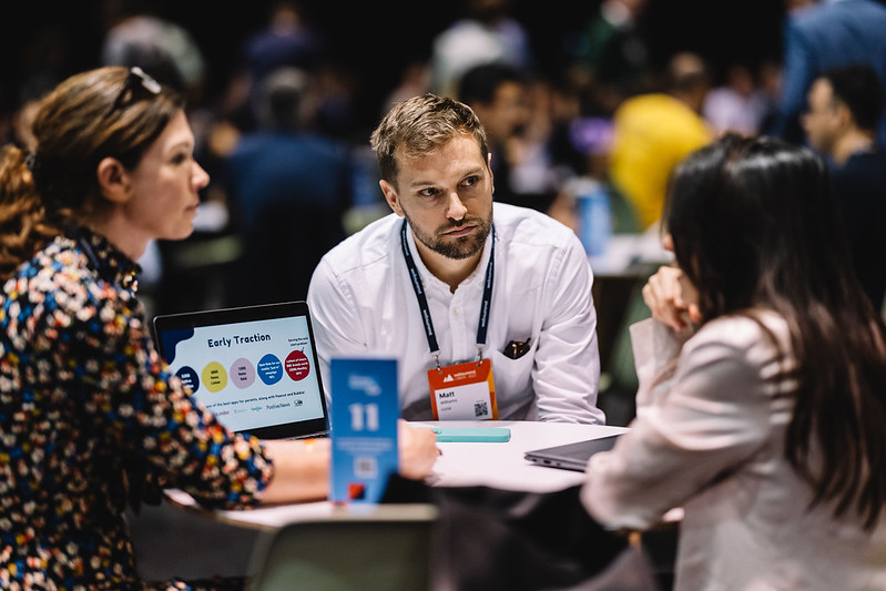 A photograph of three Web Summit attendees sitting around a table. They appear to be having a conversation.