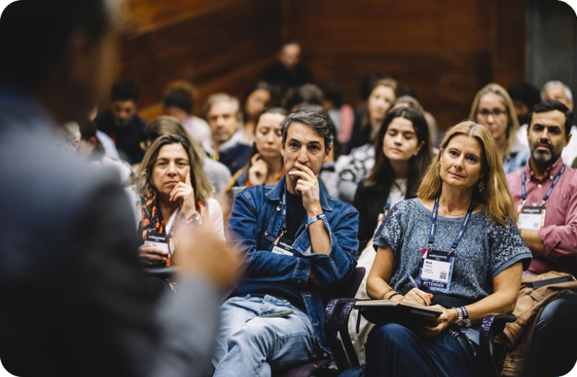 Multiple rows of seated people. They appear to be listening attentively to someone who is just visible, out of focus, in the foreground of the image.